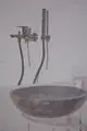 Wandmontierte Armatur in metallic Silber von Ideal Standard mit einem Handbrauseanschluss und einem Wasserabfluss in einer modernen Badezimmerumgebung.